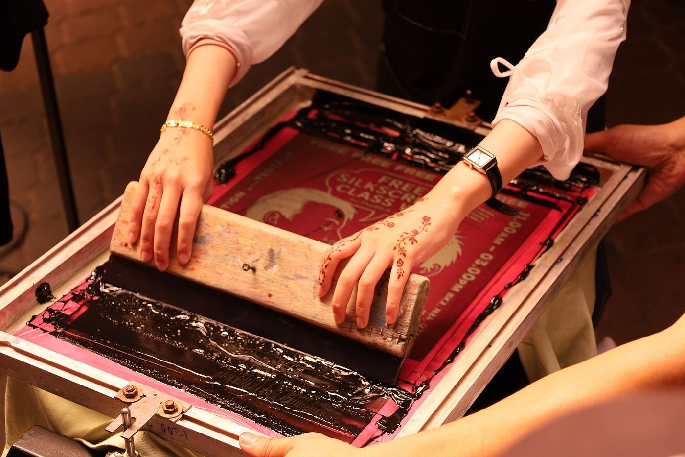 Hands pulling a squeegee across a red silkscreen frame