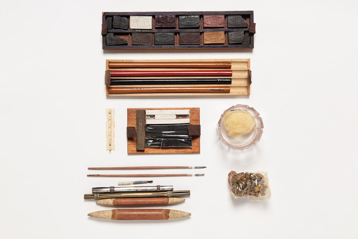 Vintage artist's box of pigments, brushes and tools laid out on white