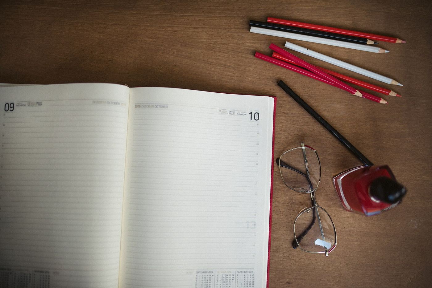 Open dated planner with coloured pencils, glasses and a bottle of ink
