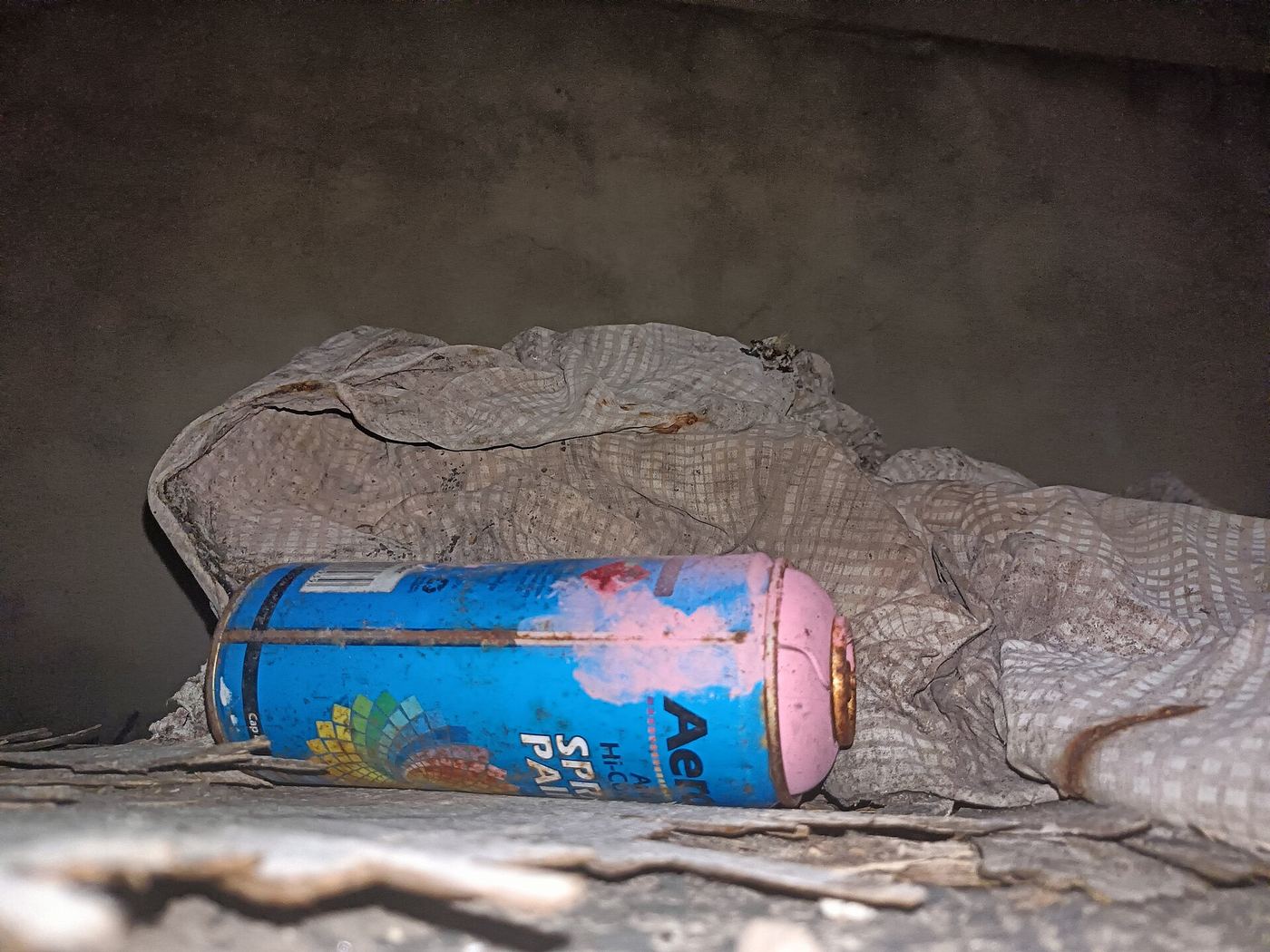 Dented blue spray-paint can lying on a dusty cloth in dim light