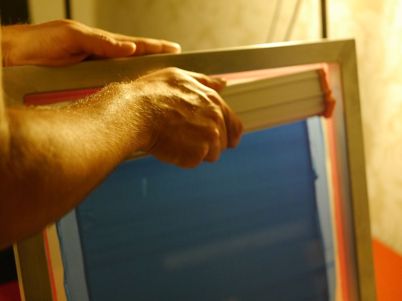 Hand holding a silkscreen frame up to warm studio light
